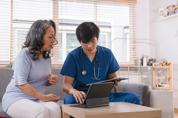 A health visitor is using a tablet to explain to a sick elderly woman how to take her pills.The visitor is taking notes on a tablet for the patient's medical interview.Home visit health care concept.