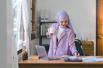 Wall Mural - Portrait of a beautiful Muslim millennial Asian businesswoman wearing a purple hijab working remotely from her home office.