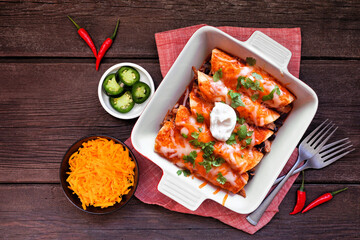 Wall Mural - Chicken enchiladas with black beans. Mexican food dish. Top view table scene on a dark wood background.