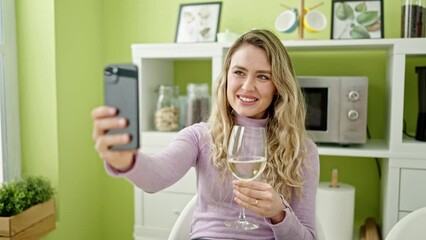 Sticker - Young blonde woman holding glass of wine having video call at dinning room