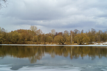  Mixed spring forest on the river bank. Birches, pines on the banks of the river. Ice drift. Spring cloudy landscape