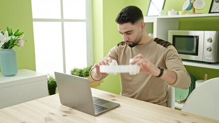 Wall Mural - Young arab man using laptop and headphones sitting on table at home