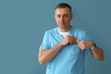 Wall Mural - Mature doctor putting bribe in pocket on blue background