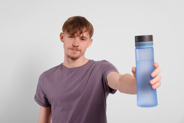 Canvas Print - Man holding transparent plastic bottle with drink on light grey background