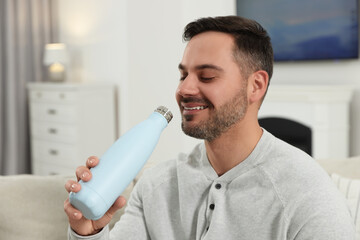 Canvas Print - Man drinking from light blue thermo bottle indoors