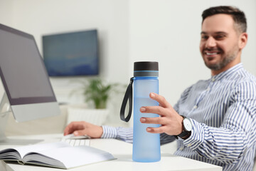 Wall Mural - Man taking transparent plastic bottle of water while working in office, focus on hand