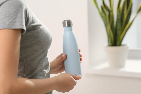 Wall Mural - Woman holding thermo bottle indoors, closeup. Space for text