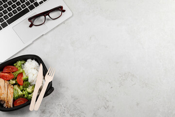 Wall Mural - Container of tasty food, laptop, cutlery and glasses on light grey table, flat lay with space for text. Business lunch