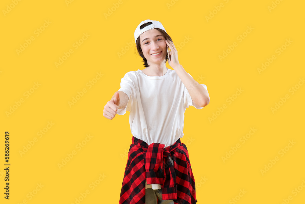 Cool teenage boy talking by mobile phone on yellow background