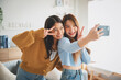 © Monster Ztudio - Two asian young women happy smiling and taking selfie in living room at home. Video call, Meeting conference