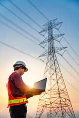 Asian electrical engineer checking position using notebook computer at power station for planning work. production of high-voltage electric poles. Vertical image.