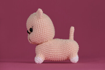 Wall Mural - Cute little crocheted cat, handmade art. Amigurumi kitten doll on pink background. A soft DIY toy made of natural cotton and wool. Side view.