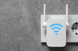 New modern repeater with Wi-Fi symbol plugged into socket on concrete wall, space for text