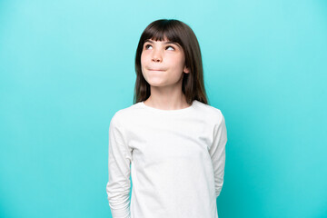 Wall Mural - Little caucasian girl isolated on blue background having doubts while looking up