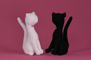 Wall Mural - Crocheted black and white kittens, handmade art. Romantic relationships between pets. Amigurumi two cats in love sitting on pink background. DIY soft toys made of natural cotton and wool.