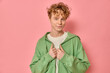 © Folenial - Fashionable young man model with red curly hair and freckles adjusting hoodie and smiling against a pink background. Happy teen feeling vibrant and cheerful while standing isolated in a studio shot.