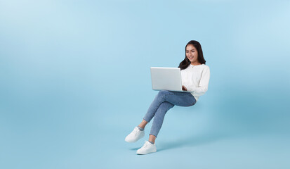 Young smiling Asian girl student floating in mid-air with using laptop isolated on blue studio copy space background.