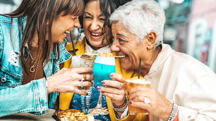 Happy senior women drinking cocktail glasses sitting at bar table - Group of best friends enjoying happy hour cheering drinks at pub restaurant - Life style concept with girls hanging out together