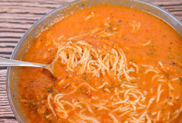 Sticker - Tomato soup with noodles being eaten with spoon on a wooden background	