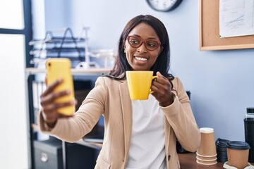 Wall Mural - Young african american woman business worker make selfie by the smartphone drinking coffee at office