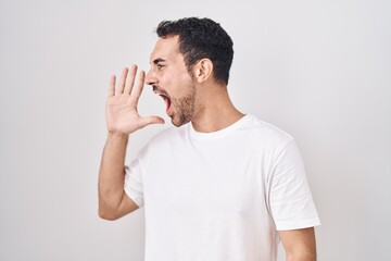 Sticker - Handsome hispanic man standing over white background shouting and screaming loud to side with hand on mouth. communication concept.