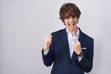 Canvas Print - Hispanic business young man wearing glasses very happy and excited doing winner gesture with arms raised, smiling and screaming for success. celebration concept.