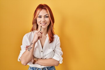 Sticker - Young caucasian woman standing over yellow background holding pen smiling with a happy and cool smile on face. showing teeth.