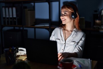 Wall Mural - Young caucasian woman working at the office at night looking away to side with smile on face, natural expression. laughing confident.