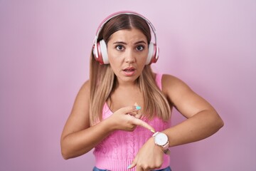 Poster - Young blonde woman listening to music using headphones in hurry pointing to watch time, impatience, upset and angry for deadline delay