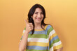 © Krakenimages.com - Middle age hispanic woman standing over yellow background doing happy thumbs up gesture with hand. approving expression looking at the camera showing success.