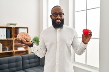 Sticker - African american man working at therapy office holding brain and heart smiling with a happy and cool smile on face. showing teeth.