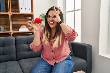 Wall Mural - Young hispanic woman working on couple therapy at consultation office smiling happy doing ok sign with hand on eye looking through fingers