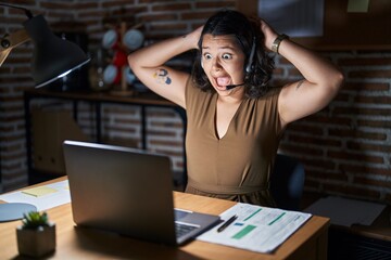 Poster - Young hispanic woman working at the office at night crazy and scared with hands on head, afraid and surprised of shock with open mouth