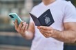 © Krakenimages.com - Young caucasian man using smartphone holding passport at street