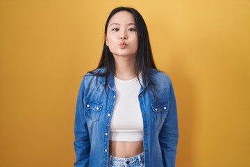 Canvas Print - Young asian woman standing over yellow background looking at the camera blowing a kiss on air being lovely and sexy. love expression.