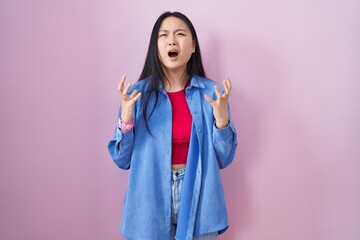 Canvas Print - Young asian woman standing over pink background crazy and mad shouting and yelling with aggressive expression and arms raised. frustration concept.