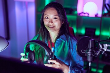 Canvas Print - Young chinese woman streamer using computer holding headphones at gaming room