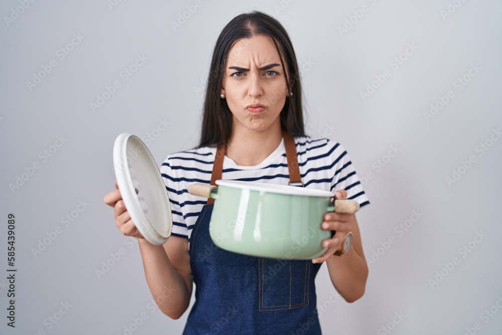 Young brunette woman wearing apron holding cooking pot skeptic and nervous, frowning upset because of problem. negative person.