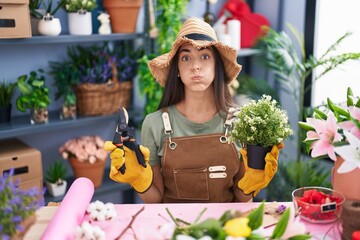 Sticker - Young brunette woman working at florist shop puffing cheeks with funny face. mouth inflated with air, catching air.