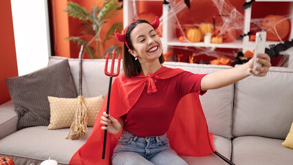 Wall Mural - Young beautiful hispanic woman wearing devil costume make selfie by smartphone at home