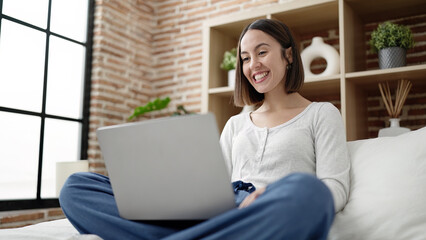 Poster - Young beautiful hispanic woman using laptop sitting on bed at bedroom