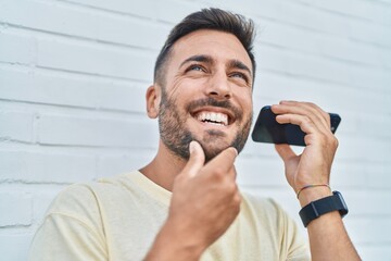 Wall Mural - Young hispanic man smiling confident listening audio message by the smartphone over isolated white background