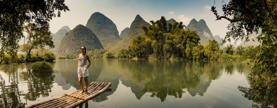 girl standing on a raft on a yalong river with beautiful scenery of limestone peaks, yangshuo, china