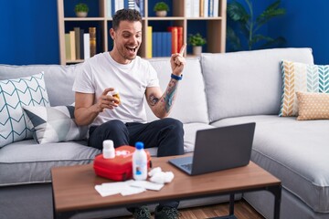 Poster - Young hispanic man watching video on laptop on how to use first aid kit smiling happy pointing with hand and finger to the side