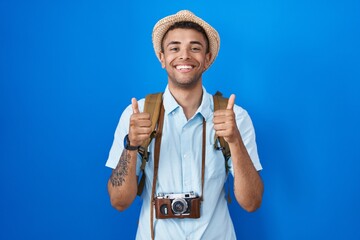 Sticker - Brazilian young man holding vintage camera success sign doing positive gesture with hand, thumbs up smiling and happy. cheerful expression and winner gesture.