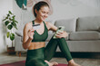 © ViDi Studio - Happy young strong athletic fitness trainer instructor woman wear green tracksuit use mobile cell phone credit card pay online train do exercises at home gym indoor Workout sport motivation concept