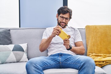 Wall Mural - Young hispanic man playing video game on smartphone at home