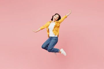 Wall Mural - Full body side view excited young woman of Asian ethnicity wear yellow shirt white t-shirt jump high with outstretched hands look camera isolated on plain pastel light pink background studio portrait.