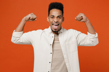 Wall Mural - Young man of African American ethnicity wear light shirt casual clothes showing biceps muscles on hand demonstrating strength power isolated on orange red background studio portrait Lifestyle concept