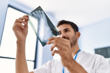 Wall Mural - Young hispanic man wearing physiotherapist uniform holding xray at clinic